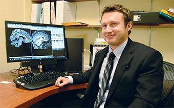 Adam Craig at his desk with brain scans on his computer monitor.