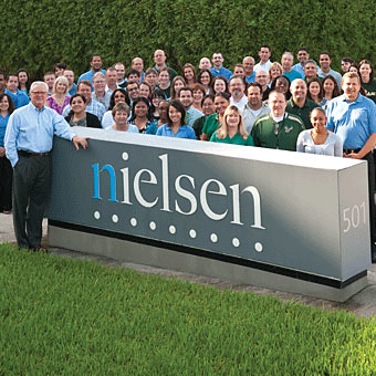 Large group of Nielsen employees, several wearing USF shirts, stand by a Nielsen sign.