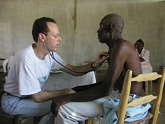 Paul Farmer holds a stethoscope up to a man's chest.