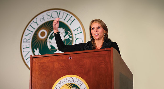 Lara Logan motions with her hand while standing at a lectern.