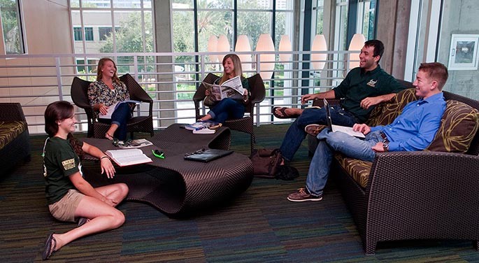 Five students sit on couches and chairs in a common area in the University Student Center.