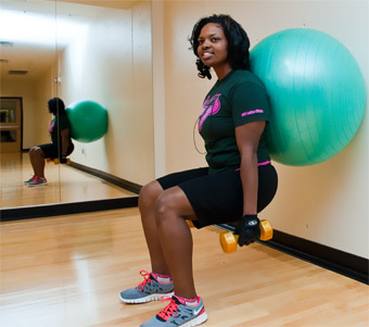 Nilesia Hall holds weights while leaning against an exercise ball.