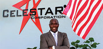 Greg Celestan stands in front of a building with the words Celestar Corporation on a wall behind him.
