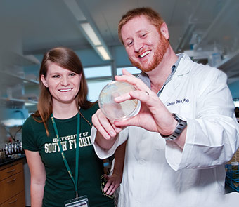 Professor Lindsey Shaw holds a petri dish while a student looks on.