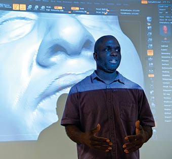 Professor McArthur Freeman II speaks in front of a display showing a 3-D model of a head.