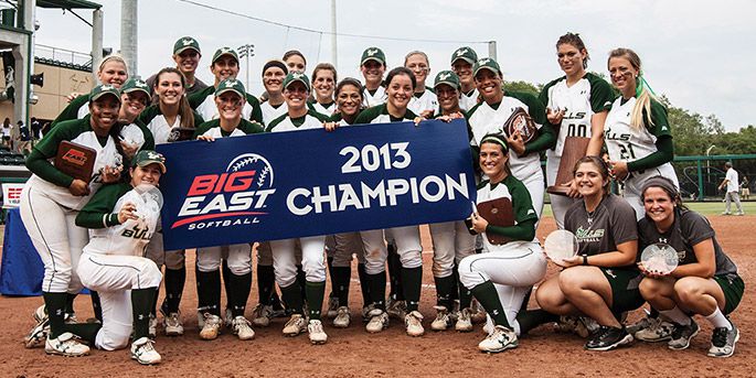 The USF softball team stands on the field holding trophies and a large sign that reads Big East Softball 2013 Champion.